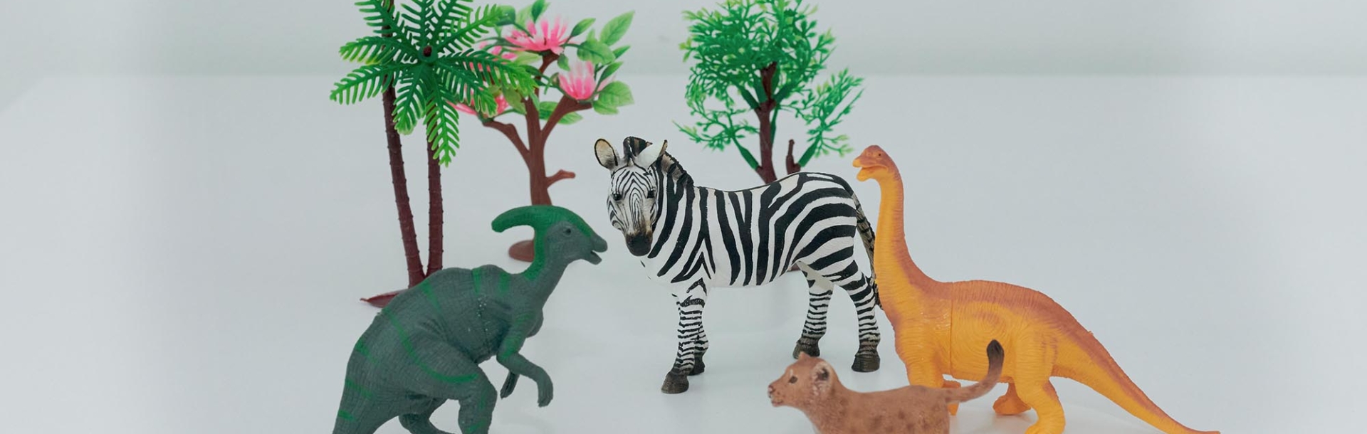 Tierfiguren für das Spiel in der Kindertherapie: Dinosaurier, Zebra und Löwe zwischen Spielzeugbäumen